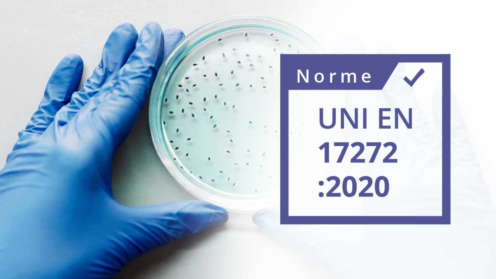 Logo norme UNI NF EN 17272 écrit dans un carrer blanc avec un contour violet. le fond de l'image est une photo d'une boite de pétrie avec des bactéries tenu par une main dans un gant en latex 