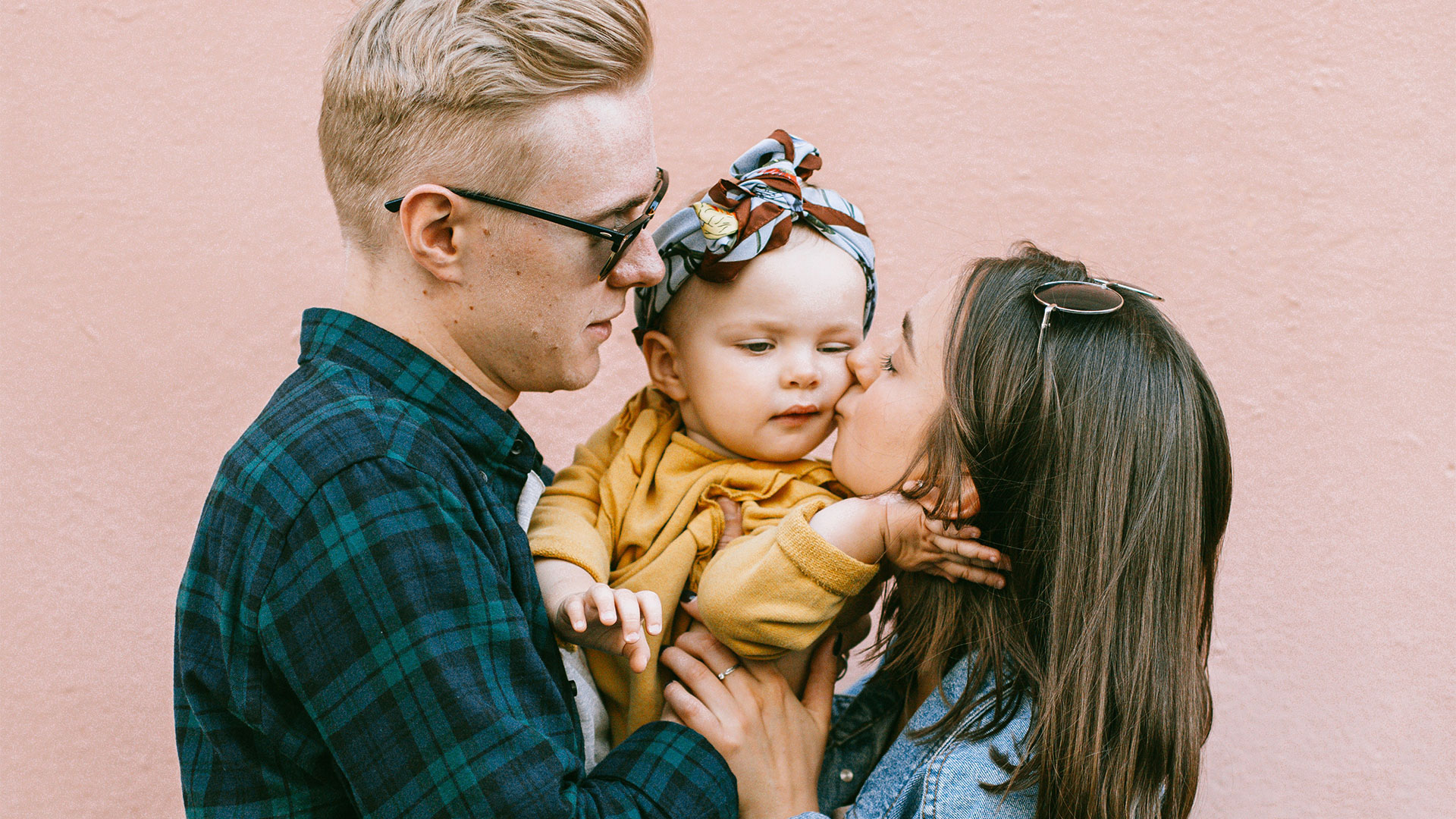 Une image montrant deux parents qui font un bisous à leur enfant.