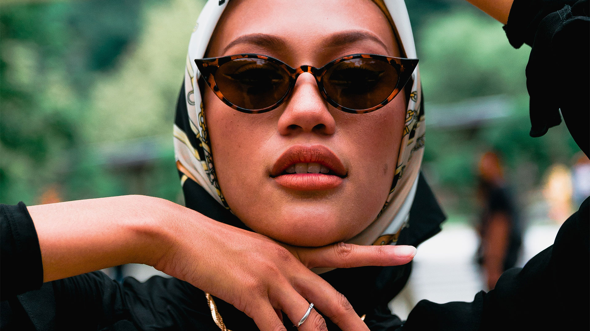 Une dame avec les cheveux entourés par un foulard et des lunettes de soleil.