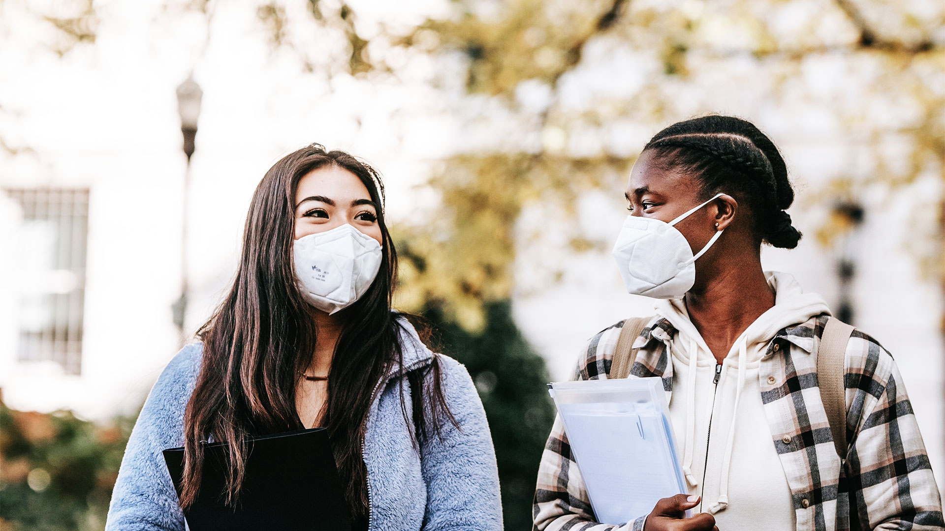 Une image qui montre deux femmes dehors en train d'échanger et qui portent un masque chirurgical