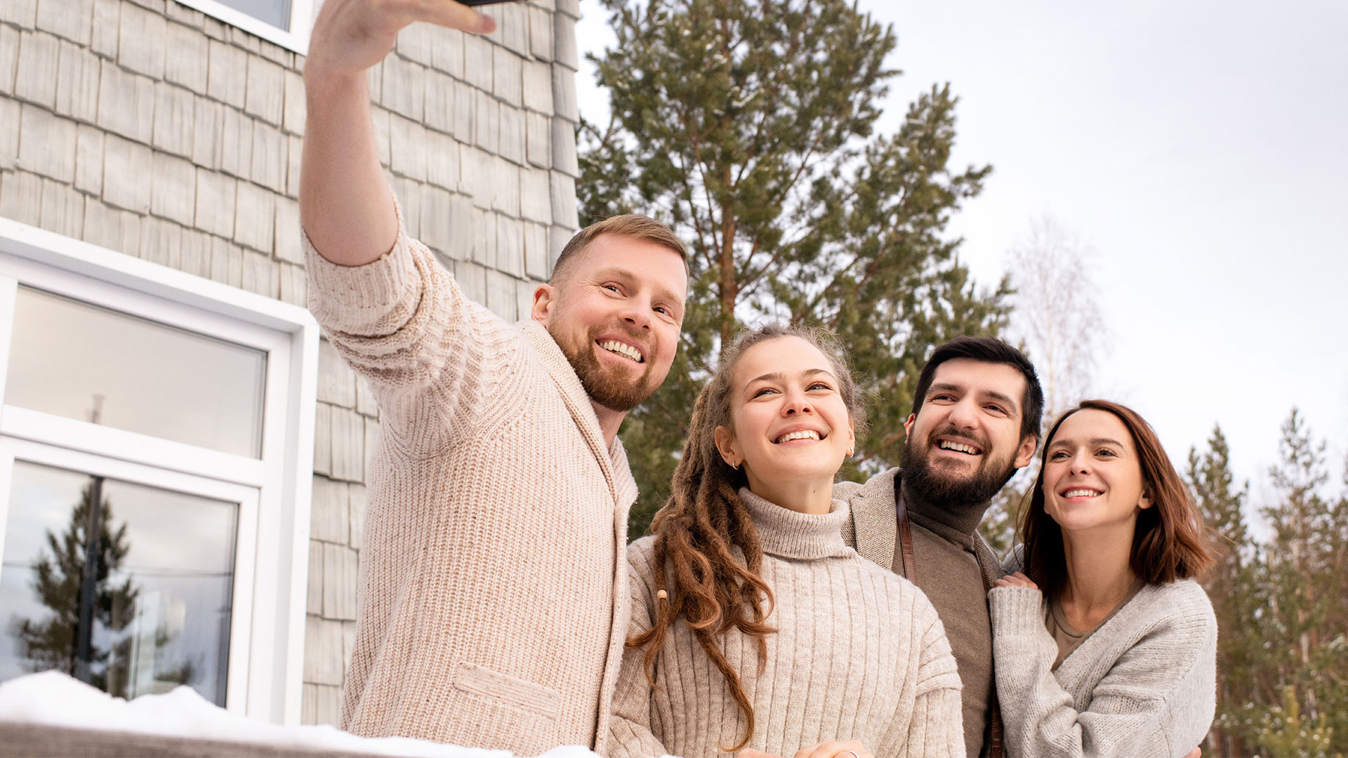 Une photo de 4 personnes qui se prennent en photos et en arrière plan un maison et des arbres.