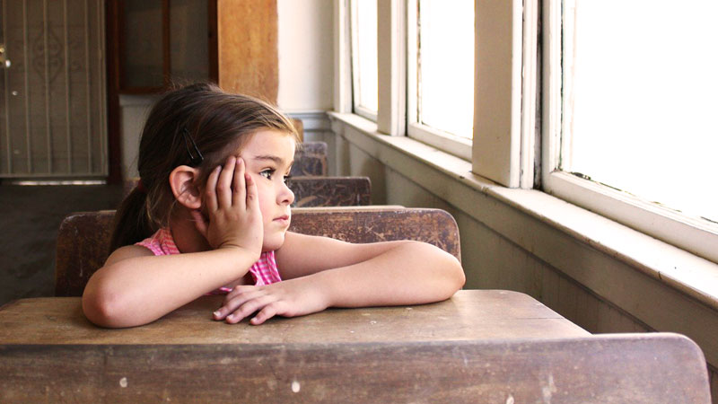 aeration fille a l'ecole sur son bureau devant une fenêtre regarde au loin pensive