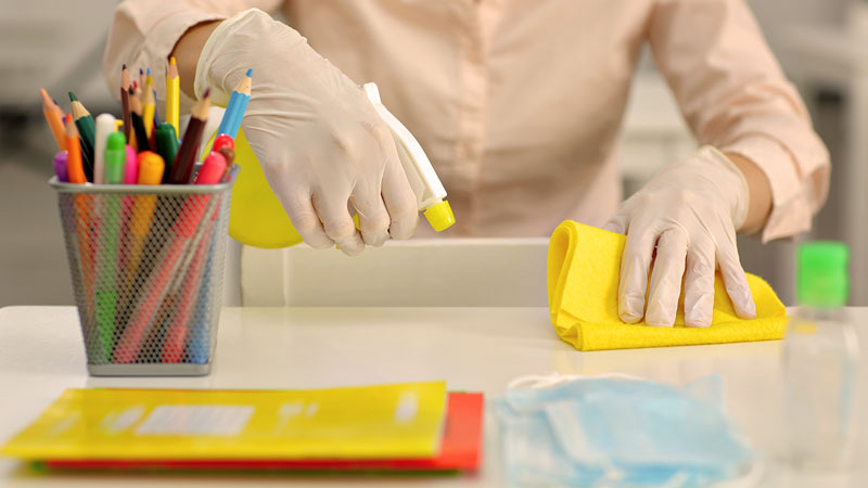 décontamination des surfaces dans l'education, une personne nettoie un bureau avec du produit