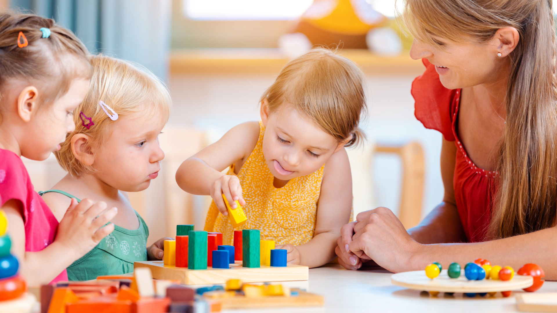 enfant qui joue avec une assistante maternel à empiler des cube de couleur