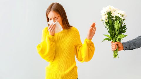 Une femme avec un pull jaune qui repousse les fleurs que lui offrent son mari car elle est allergique.