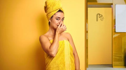 femme se bouchant le nez en serviette jaune devant une porte de douche.