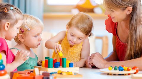 enfant qui joue avec une assistante maternel à empiler des cube de couleur 